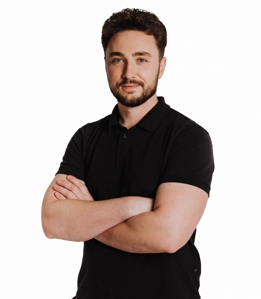 Ein Mann mit kurzen braunen Haaren und einem Bart, der ein schwarzes Polohemd mit dem Logo des Malerfachbetriebs Stein trägt, steht mit verschränkten Armen und einem leichten Lächeln vor einem weißen Hintergrund vor der Kamera.